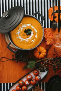 Zupa dyniowa w garnku z kremem i natką, na halloweenowym stole z dekoracjami