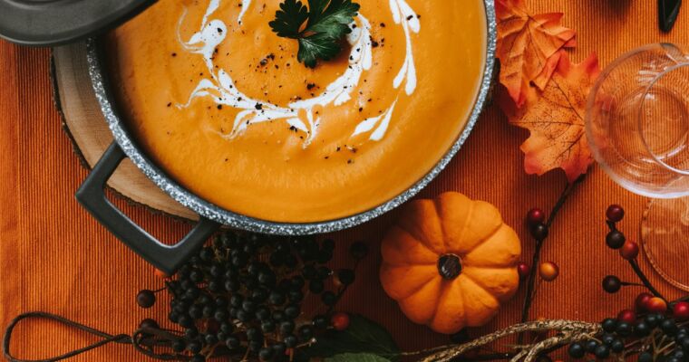 Zupa dyniowa w garnku z kremem i natką, na halloweenowym stole z dekoracjami